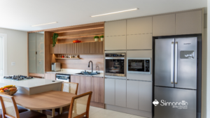 Cozinha planejada Simonetto com armários fendi e madeira natural, integrada com mesa e eletros embutidos