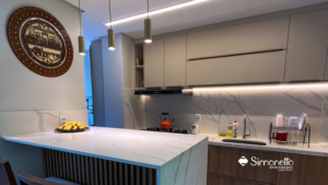 Cozinha planejada com armários bege, iluminação embutida e bancada marmorizada